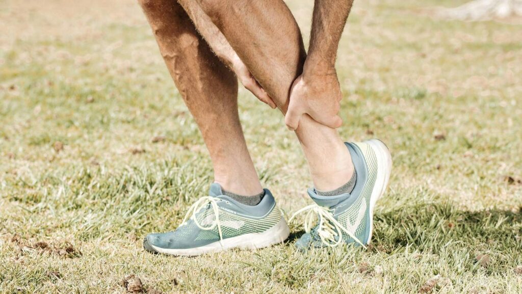 A runner holds his ankle in pain, a sign of an injury that may require a visit to an emergency podiatrist in Houston.