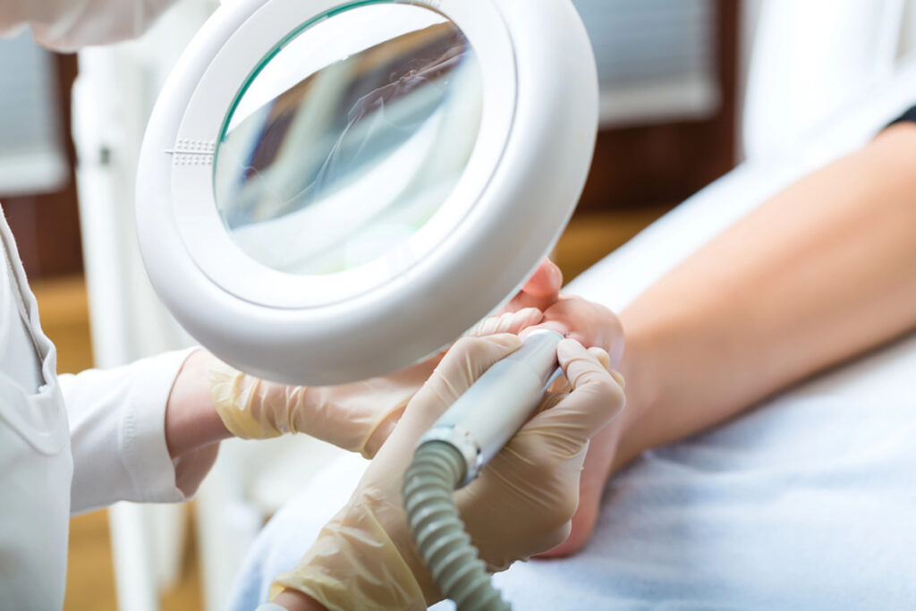 Gloved professional performing precise nail care under magnifying lamp, hygienic tools — Foot And Ankle Specialist 
