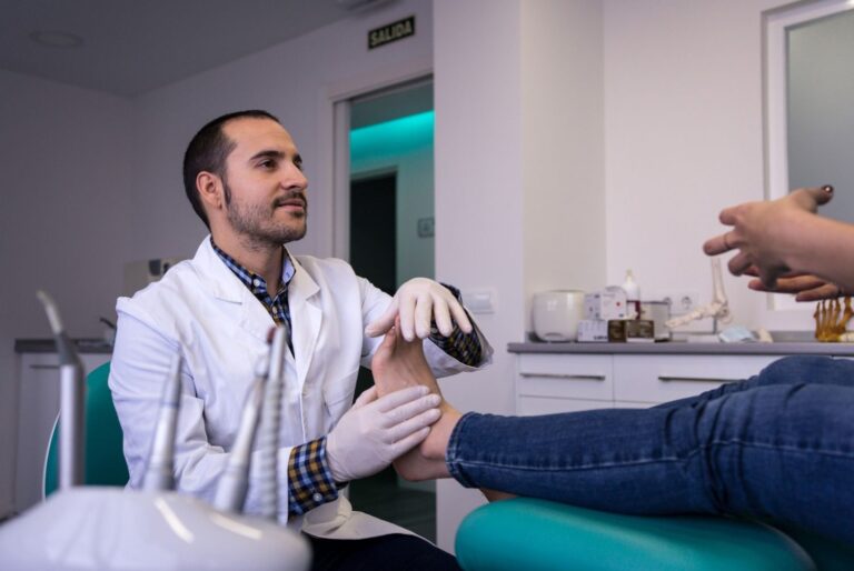 Podiatrist wearing a white coat and gloves examines a patient's foot; expert Amerigroup podiatrist Cypress.