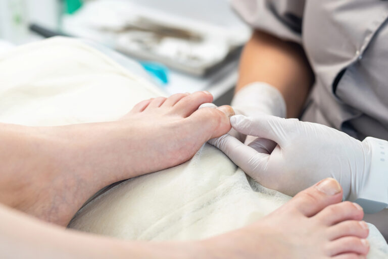 Gloved podiatrist examining big toenail for infection or ingrown issues, precise foot care in a podiatry clinic.
