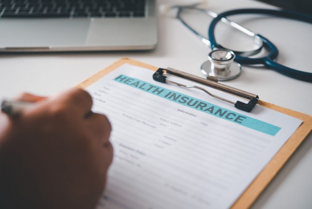 Person signing a Health Insurance form near a laptop; find an accepted blue cross blue shield podiatrist cypress today.