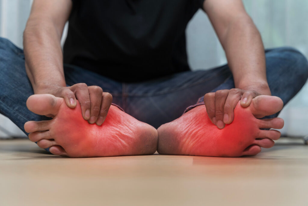 Person sitting on floor holding both feet in pain. Heel Pain Doctor Cypress treats chronic plantar discomfort.
