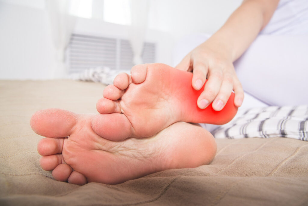 Close up of hand massaging a sore heel on a bed. Consult a Heel Pain Doctor Cypress for expert podiatry care.