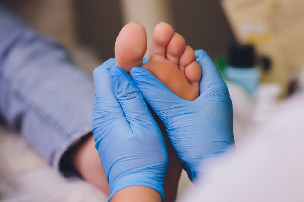 A podiatrist at Superior HealthPlan Cypress performs a foot examination on a patient's arch, using blue nitrile gloves.