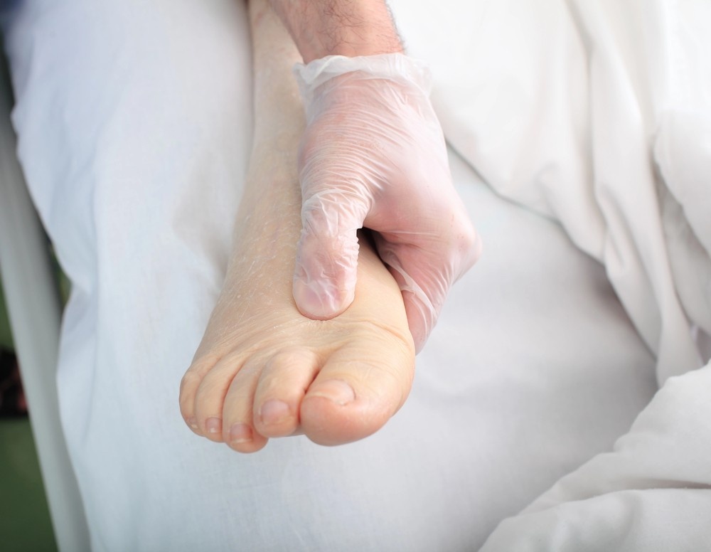 Superior HealthPlan podiatrist Cypress examines a foot, pressing on the top with a gloved hand, on a white medical bed.