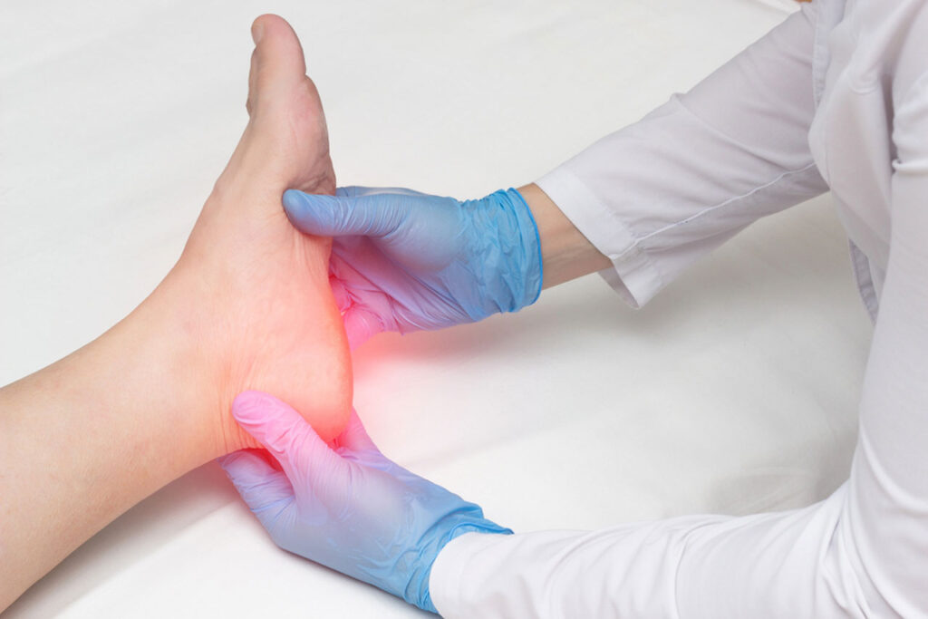 Hands with blue gloves perform a physical exam on a patient's sore heel by a leading heel pain doctor Cypress.