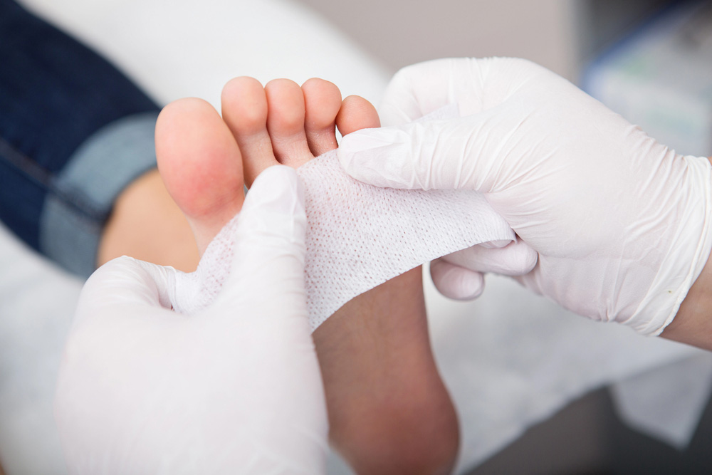 Gloved hands applying medical gauze to a patient's foot, a procedure at a Blue cross blue shield podiatrist cypress clinic.